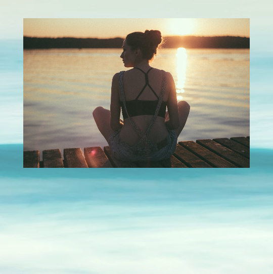 image of woman sitting cross legged at sunset looking at lake
